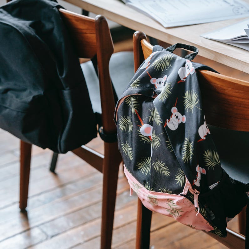 School desk with opened copybooks textbooks and stationery near chairs with backpack in light modern classroom